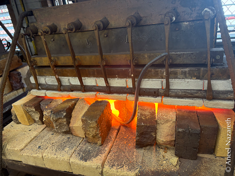 A curved bar protrudes somewhat awkwardly from a gas-powered forge surrounded by firebrick